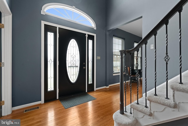 foyer entrance with a healthy amount of sunlight, wood-type flooring, visible vents, and stairs