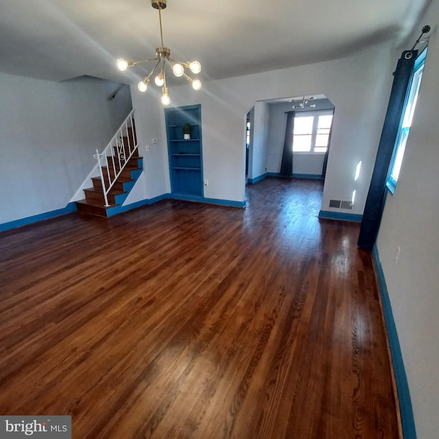 unfurnished living room featuring wood finished floors, visible vents, an inviting chandelier, and stairs