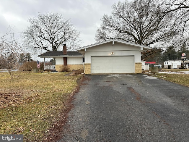 view of front of home featuring aphalt driveway, an attached garage, brick siding, a chimney, and a front yard