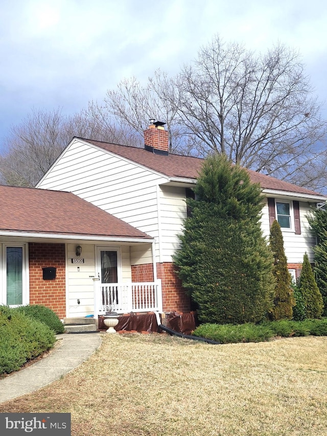 view of front of home featuring a porch, a front yard, a shingled roof, brick siding, and a chimney