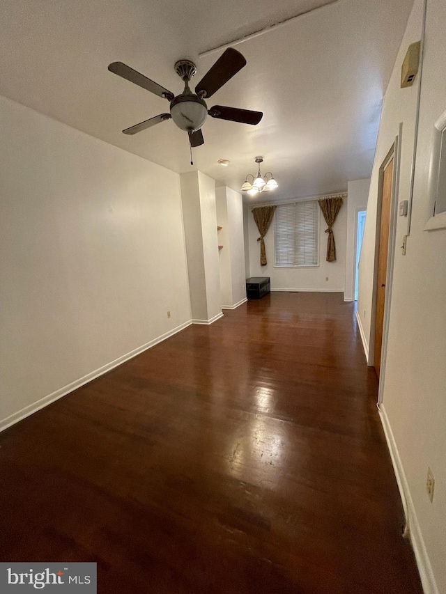 unfurnished living room featuring ceiling fan with notable chandelier, dark wood finished floors, and baseboards