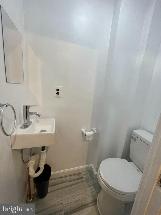 half bath featuring a sink, wood finished floors, toilet, and baseboards