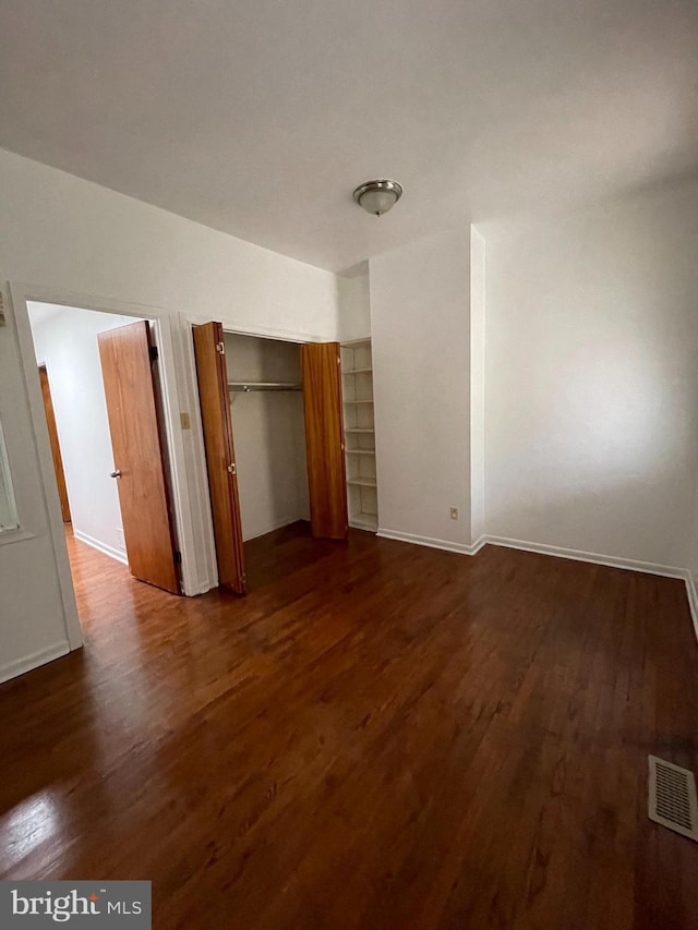 unfurnished bedroom with a closet, dark wood finished floors, visible vents, and baseboards