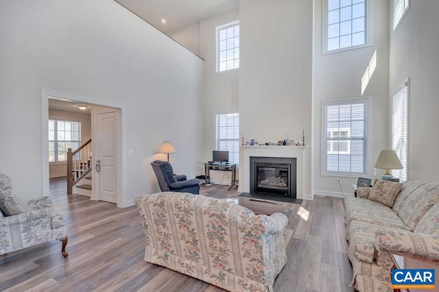 living area with stairs, a fireplace with flush hearth, wood finished floors, and baseboards