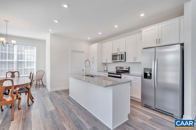 kitchen featuring white cabinets, appliances with stainless steel finishes, a sink, a kitchen island with sink, and a notable chandelier