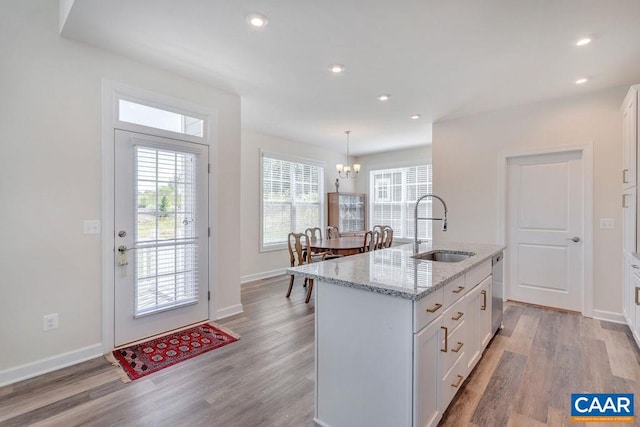 kitchen with light stone counters, light wood-style flooring, a sink, white cabinetry, and dishwasher