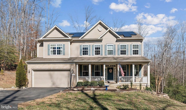 view of front of property with covered porch, solar panels, brick siding, a garage, and driveway