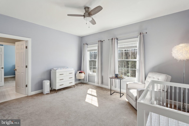 carpeted bedroom featuring a nursery area, ceiling fan, and baseboards