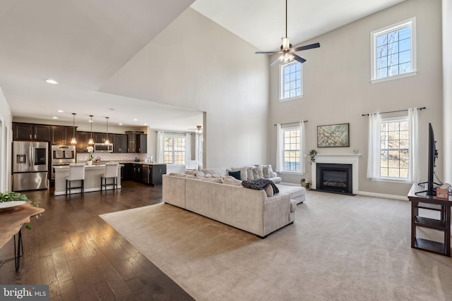 living area featuring baseboards, a fireplace with flush hearth, ceiling fan, dark wood-type flooring, and recessed lighting