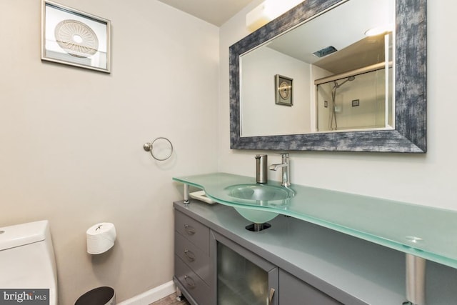 bathroom with toilet, a shower with shower door, vanity, and baseboards