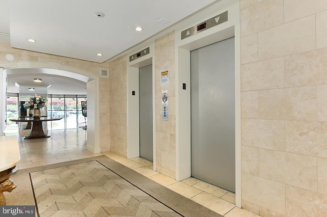 hallway featuring arched walkways, elevator, tile walls, and recessed lighting