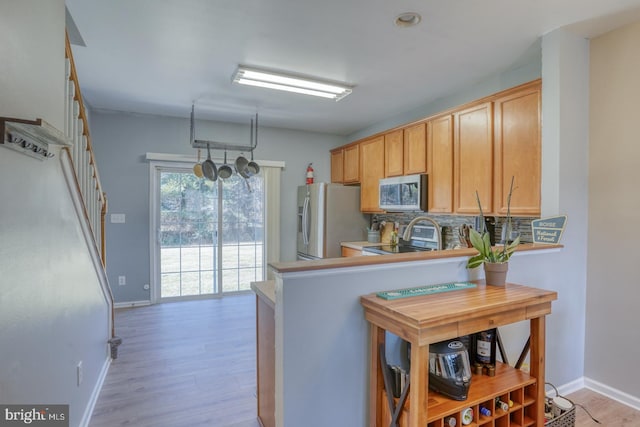 kitchen with baseboards, appliances with stainless steel finishes, backsplash, and light wood-style floors