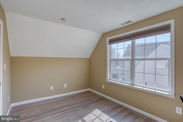 additional living space featuring vaulted ceiling, wood finished floors, visible vents, and baseboards