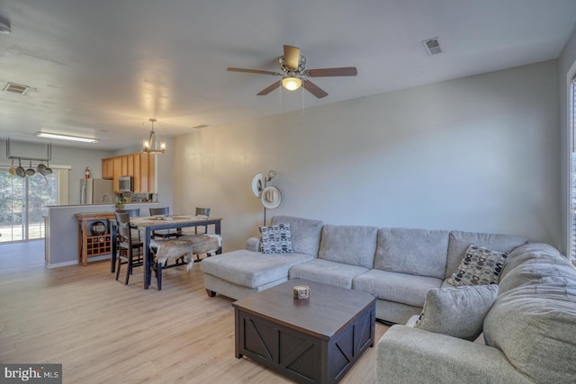 living area featuring light wood-style floors, visible vents, and ceiling fan with notable chandelier