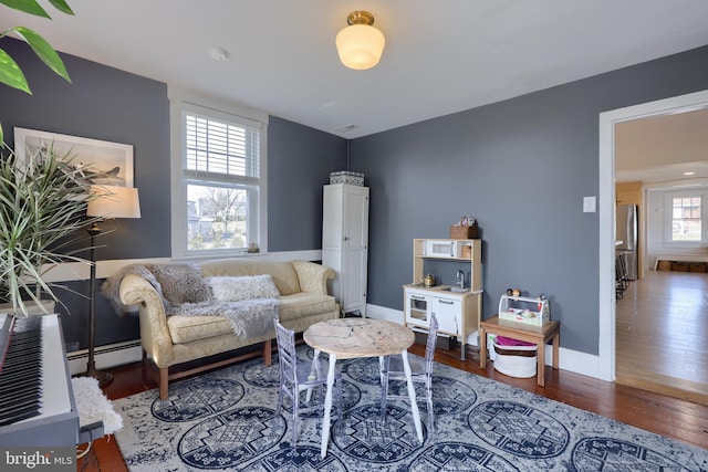 living room with a baseboard heating unit, wood finished floors, and baseboards