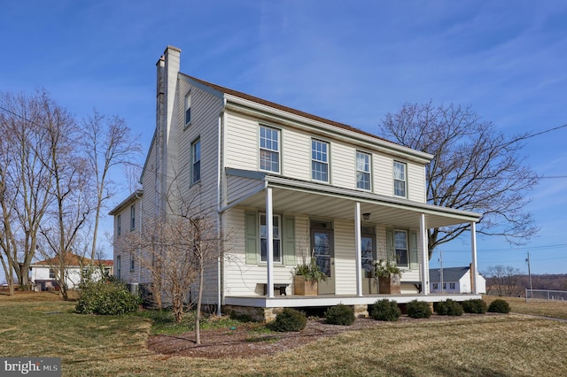 view of front of home with covered porch, a chimney, and a front lawn