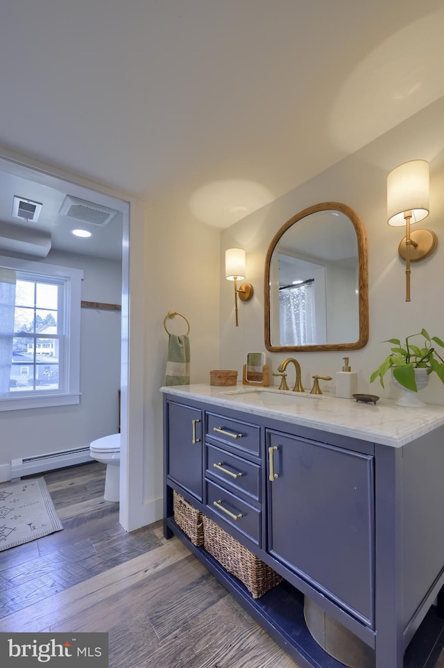 bathroom featuring visible vents, toilet, wood finished floors, vanity, and a baseboard heating unit