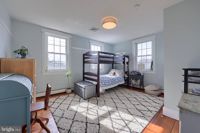 bedroom with light wood finished floors, baseboard heating, and visible vents