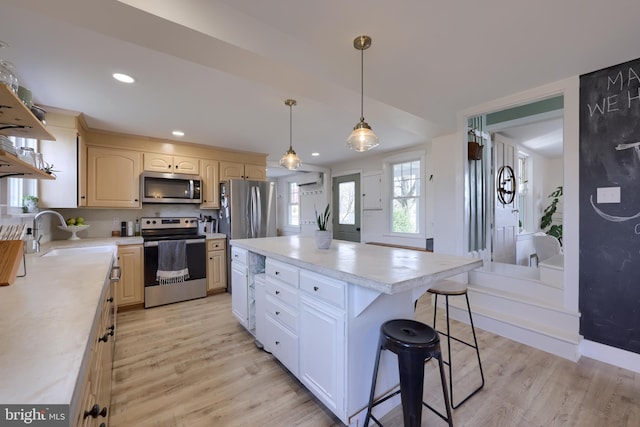 kitchen with appliances with stainless steel finishes, light countertops, a sink, and light wood finished floors