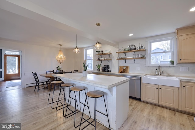 kitchen featuring light countertops, a sink, light wood-type flooring, dishwasher, and a kitchen breakfast bar