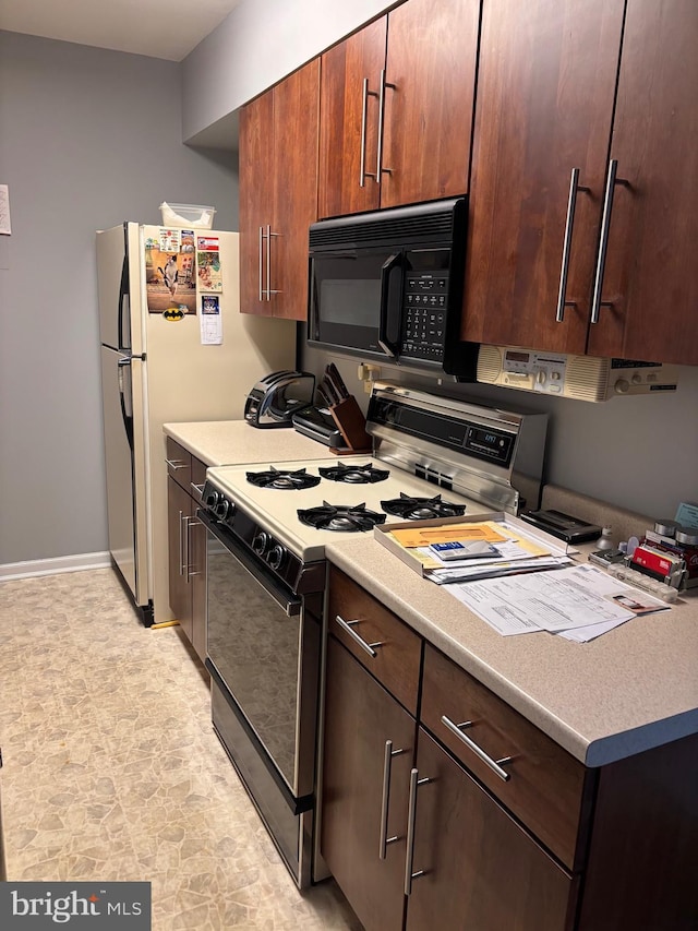 kitchen with black microwave, light countertops, gas range oven, and baseboards