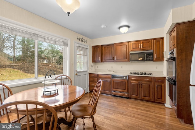 kitchen featuring brown cabinets, light wood finished floors, light countertops, a sink, and black appliances