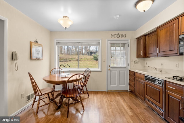 kitchen with black microwave, a sink, light countertops, light wood-type flooring, and dishwasher