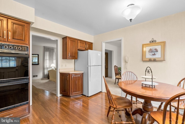 kitchen featuring dobule oven black, visible vents, brown cabinetry, freestanding refrigerator, and wood finished floors