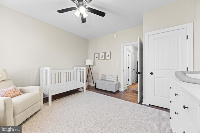 bedroom featuring ceiling fan, a nursery area, wood finished floors, and baseboards