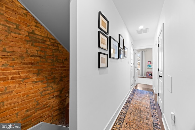 corridor with brick wall, visible vents, and baseboards