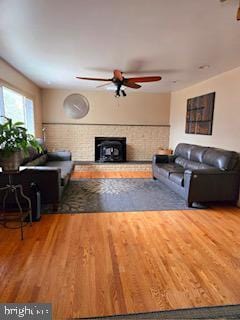 living room with a fireplace with raised hearth, wood finished floors, and a ceiling fan