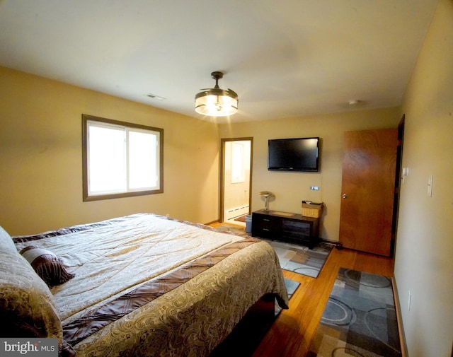 bedroom with baseboards, a baseboard heating unit, and light wood-style floors