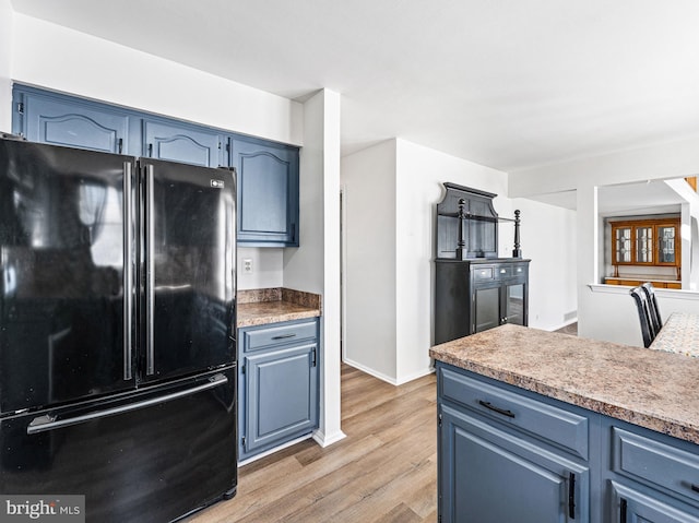 kitchen featuring light wood-style flooring, freestanding refrigerator, and blue cabinets