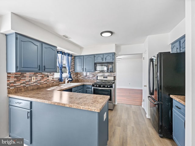 kitchen with a peninsula, black appliances, blue cabinetry, and a sink