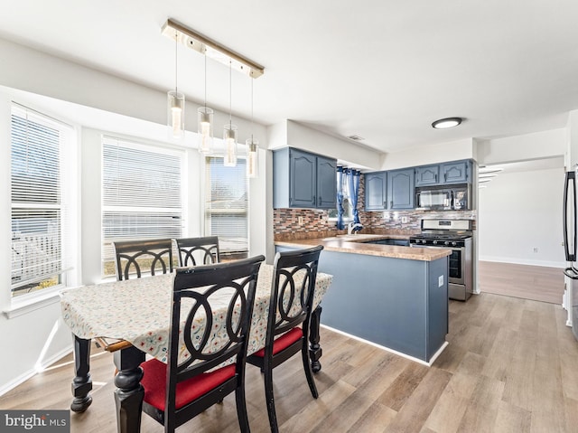 kitchen with black microwave, a peninsula, blue cabinetry, decorative backsplash, and stainless steel gas stove