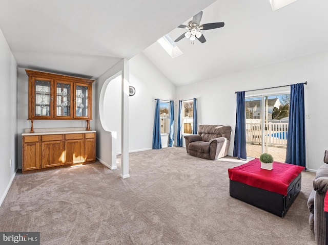 living area with carpet floors, vaulted ceiling with skylight, a ceiling fan, and baseboards