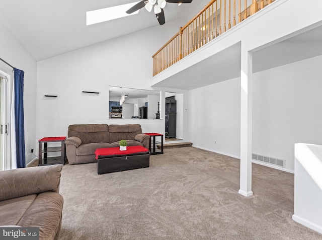 carpeted living room featuring a skylight, visible vents, a ceiling fan, high vaulted ceiling, and baseboards