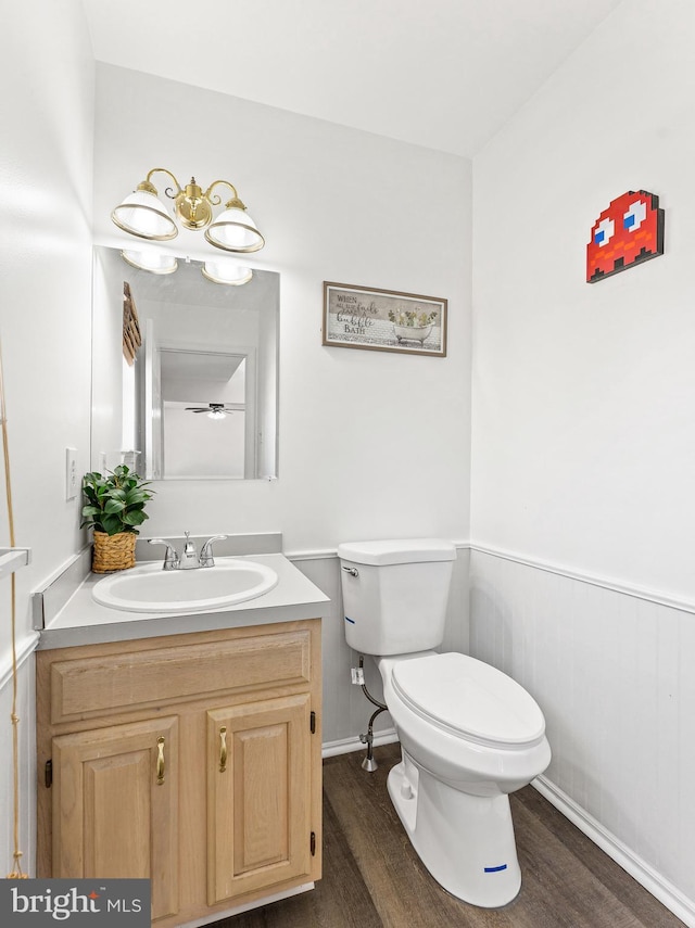 half bath with a wainscoted wall, vanity, toilet, and wood finished floors