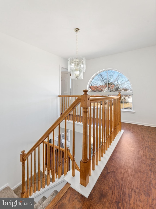 stairway featuring baseboards, wood finished floors, and a notable chandelier