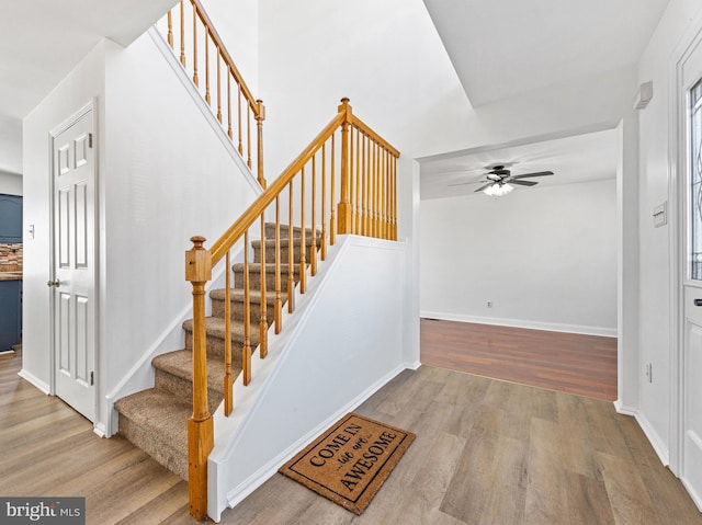 staircase with a ceiling fan, baseboards, and wood finished floors