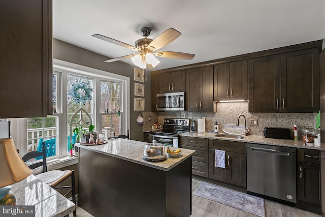 kitchen with stainless steel appliances, light stone counters, a sink, and dark brown cabinetry