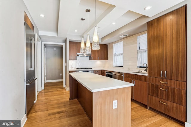 kitchen with stainless steel appliances, a kitchen island, a sink, backsplash, and light wood finished floors