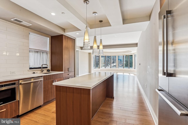 kitchen with a sink, visible vents, appliances with stainless steel finishes, brown cabinetry, and modern cabinets