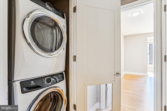 laundry area with wood finished floors, stacked washer and clothes dryer, baseboards, and laundry area