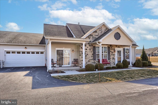 view of front of house featuring stone siding, roof with shingles, an attached garage, and driveway