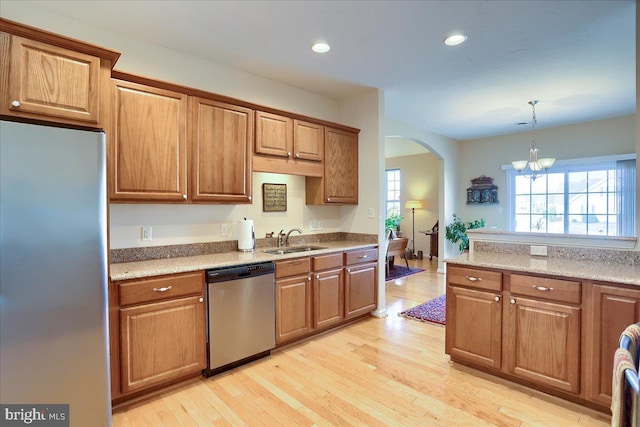 kitchen with stainless steel appliances, light wood-type flooring, a sink, and arched walkways