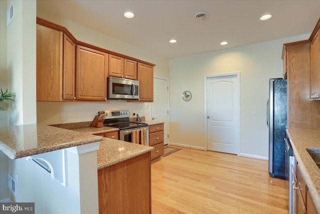 kitchen featuring appliances with stainless steel finishes, brown cabinets, a peninsula, light stone countertops, and light wood-type flooring