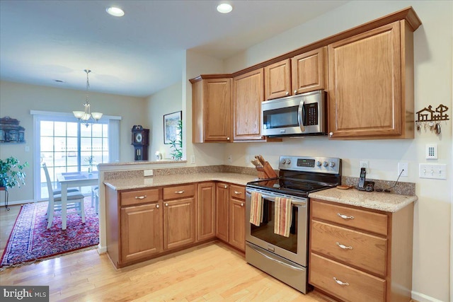 kitchen featuring stainless steel appliances, a peninsula, light stone countertops, light wood finished floors, and an inviting chandelier