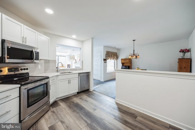 kitchen with wood finished floors, light countertops, stainless steel appliances, white cabinetry, and a sink