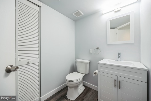 half bathroom with toilet, wood finished floors, vanity, visible vents, and baseboards